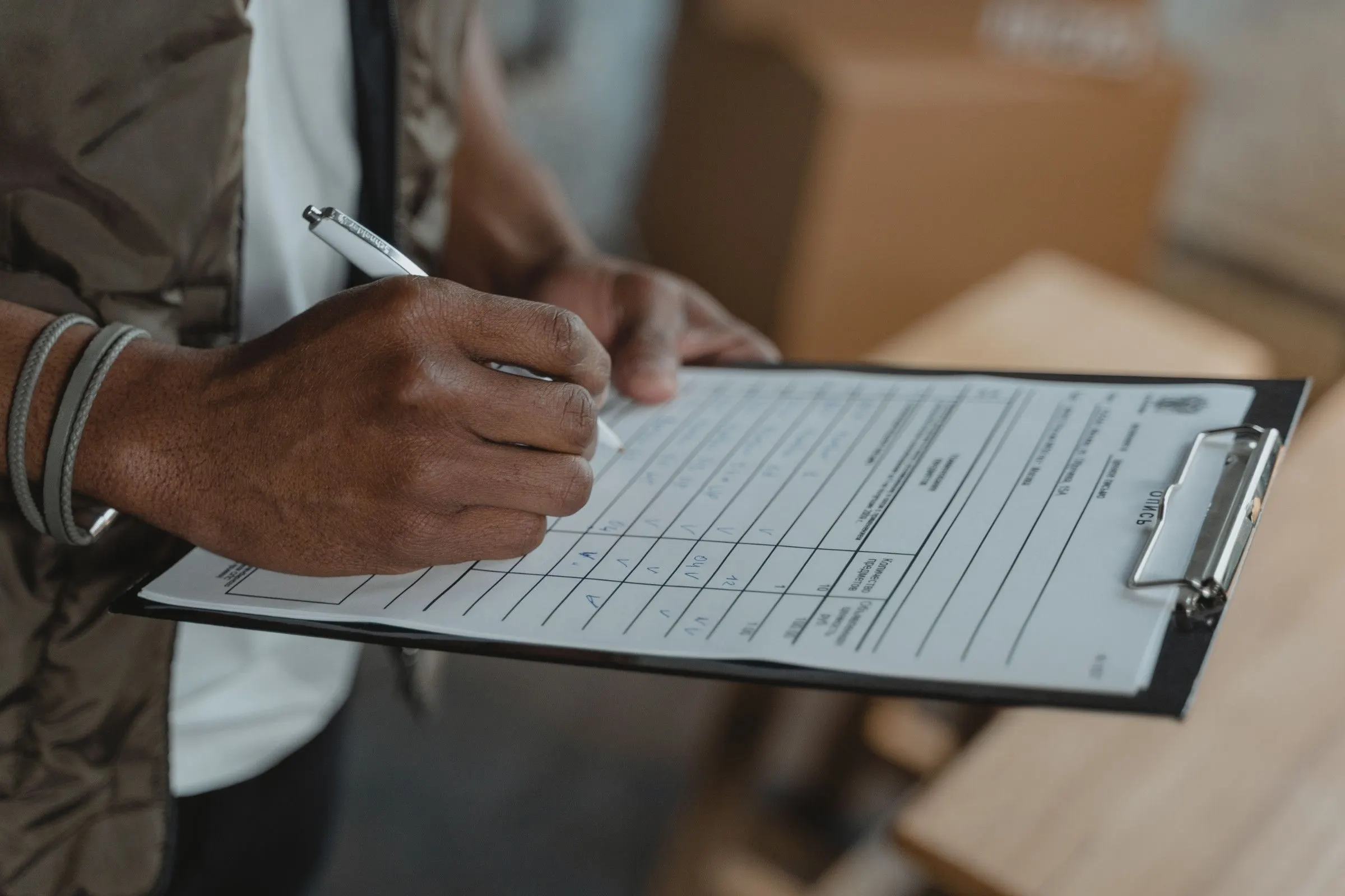 Mâini completând un formular pe clipboard, lângă marfă ambalată